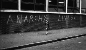 Small girl walks past the graffiti 'Anarchy Lives!'  Photo by Judy Greenway. East London, 1970s.