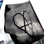 Anarchist black flag with the anarchist 'A' enclosed in a heart, and part of a rainbow flag.