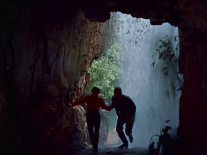  Emma and Johnny, silhouetted against the exit of a cave, pass through the waterfall into another space.