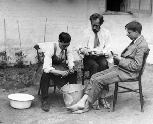 Three men peeling potatoes in garden, around 1917.